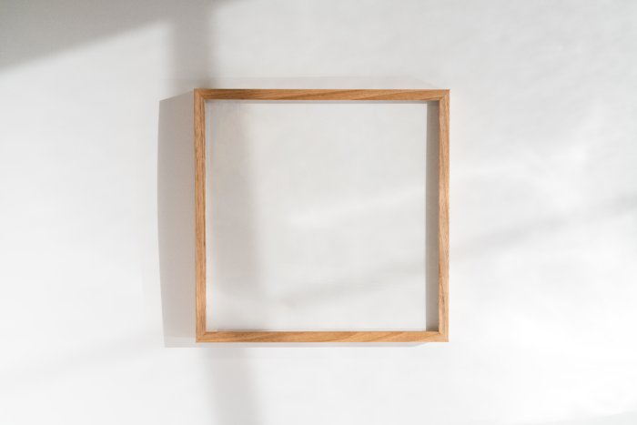 An empty wooden picture frame on a white wall