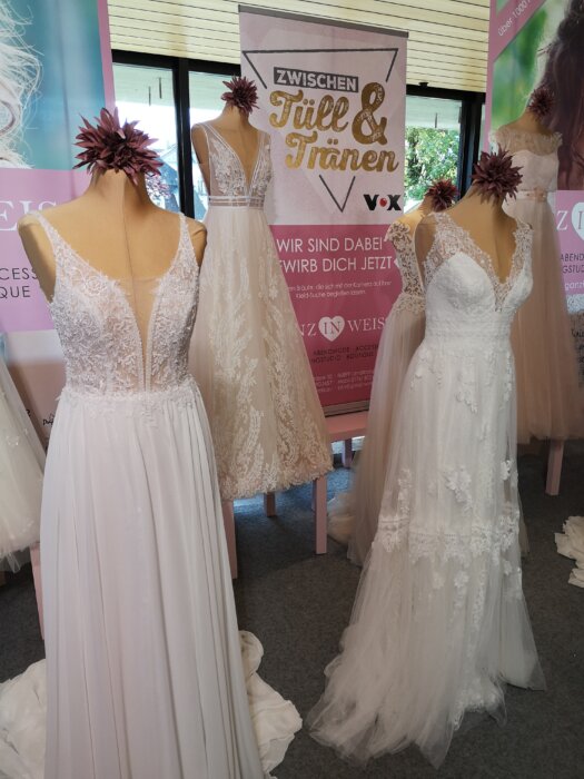 photograph of an exhibition stand of a bridal fashion boutique advertising its participation in the TV series Zwischen Tüll und Tränen showing three bridal dresses